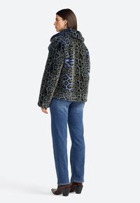 Veste en fausse fourrure grise-noire avec des taches léopard bleues, dotée d'un col montant et d'une coupe décontractée. Associée à un jean bleu à jambe droite et des talons foncés.