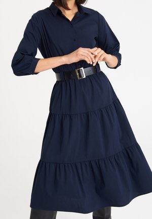 Robe évasée bleu marine en tissu léger, avec un col chemise, une fermeture à boutons sur le devant, et une large ceinture noire à boucle carrée.