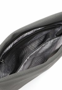 Interno di una borsa in pelle grigio perforata con foderatura in satin liscia, dotata di una tasca con zip e una leggera marcatura in un motivo ripetuto.