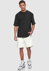 T-shirt noir oversize, shorts en mesh blanc et baskets blanches. Comprend des détails de poignets côtelés et des textures contrastées sur la tenue.
