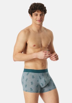 Blå boxershorts för män med ananasmönster, gjorda av mjukt tyg, med en kontrasterande midjeresår och en figurnära design.