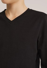 Fekete pamut hosszú ujjú póló V-nyakú kialakítással, sima textúrával és testhezálló sziluettel.