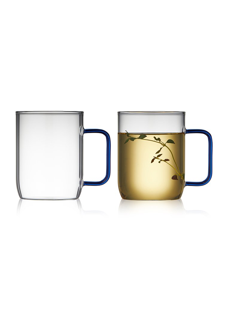 Dwa szklane kubki z niebieskimi uchwytami; jeden jest pusty i przezroczysty, a drugi wypełniony żółtym płynem, z widocznymi ziołami w środku.