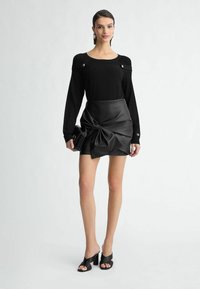 Zwarte gebreide trui met schouderdetails, gecombineerd met een hooggetailleerde leren minischoot met een geknoopte accent. Zwarte open teen hakken.