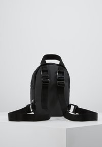 Svart ryggsäck med texturerad, vadderad yta, dubbla handtag, justerbara remmar och silverfärgade detaljer. Kompakt design och robust konstruktion.