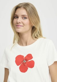 Camiseta de algodón blanca con un gran diseño de flor roja con detalles en negro en el centro. Cuello redondo, mangas cortas.