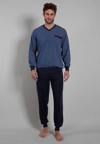 Herren-Loungewear-Set bestehend aus einem langärmeligen Oberteil in Blau mit Muster und rotem Kragen sowie einer Tasche, kombiniert mit einfarbigen navyblauen Hose mit elastischem Bund.