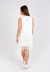 White sleeveless dress featuring intricate lace cutouts at the hem. The design includes a round neck and a back keyhole detail.
