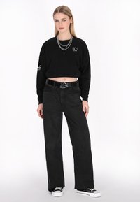 Felpa nera corta con grafiche bianche, abbinata a jeans neri a vita alta e gamba larga, e sneakers nere con suola bianca. Collana in argento.