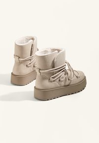 Beige Kunstwildleder-Stiefeletten mit einem weichen Innenfutter, einer dicken Plattformsohle und Schnürdetails, ausgestattet mit einer strukturierten Gummisohle.