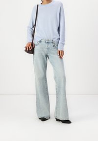 Suéter de punto azul claro con mangas largas, combinado con unos vaqueros de pierna ancha de lavado claro a la cintura, y terminado con zapatos de tacón negros.