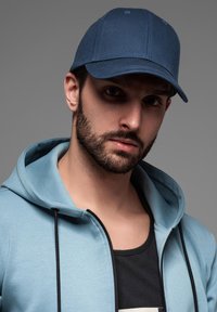 Blå stofkappe med en buet skygge og syede sømme, parret med en lyseblå hoodie med en sort lynlås og snore.