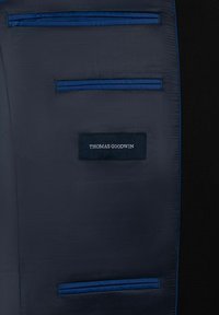 Innenseite eines marineblauen Sakkos aus glattem Stoff; verfügt über drei Taschen und ein Etikett mit "THOMAS GOODWIN" in weißem Text auf einem schwarzen Rechteck.
