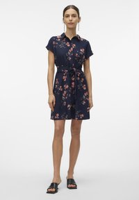 Vestido camisa azul marinho com padrão floral, mangas curtas, frente com botões e cintura com cinto. Tecido suave com uma textura leve.