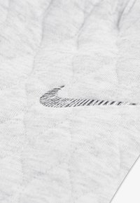 Υφασμα σε ανοιχτό γκρι χρώμα με υφή καπιτονέ, που φέρει το μαύρο λογότυπο της Nike ραμμένο σε καμπύλο σχήμα. Καθαρός και μινιμαλιστικός σχεδιασμός.