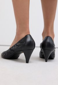 Black leather high-heeled shoes with a tapered design, gathered material at the heel, and a slightly glossy finish.