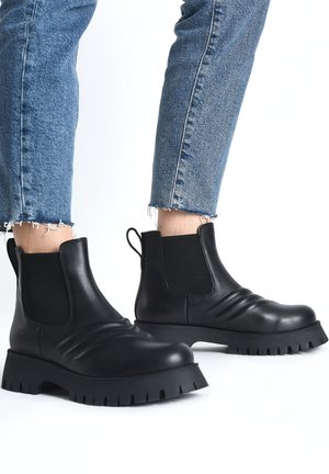Sorte Chelsea-støvler i læder med elastiske sidepaneler, kraftige gummisåler og en rillede tekstur, kombineret med korte denimjeans.