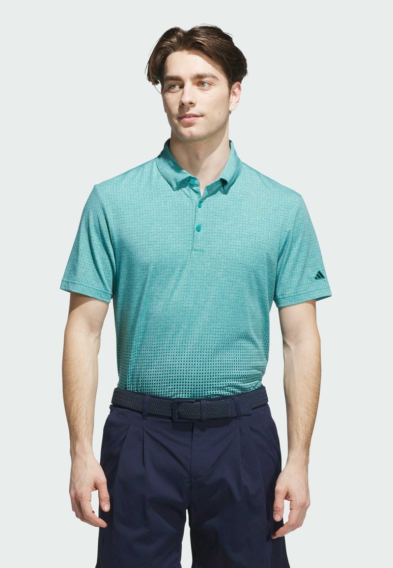 Teal väri polo paita, jossa on täplätumma kuvio, lyhyet hihat ja kolmonen nappilista. Yhdistetty tummansinisiin housuihin ja teksturoituun vyöhön.