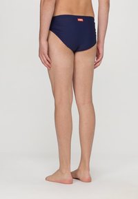 Slip da mare blu navy con una texture liscia, taglio basso e un piccolo logo arancione sul retro. Adatti per attività acquatiche.