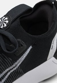 Gros plan d'une chaussure de course Nike noire avec des coutures blanches, des lacets noirs et une semelle blanche, montrant le col de la chaussure et les détails du logo.