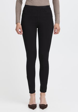 Czarne legginsy rozciągające się z wysokim stanem, o gładkiej teksturze i dopasowanym kroju, kończące się tuż nad kostką.