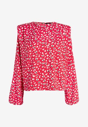 Blouse rouge à manches longues avec des taches irrégulières en forme de cœur en blanc et noir, et des épaules légèrement bouffantes.
