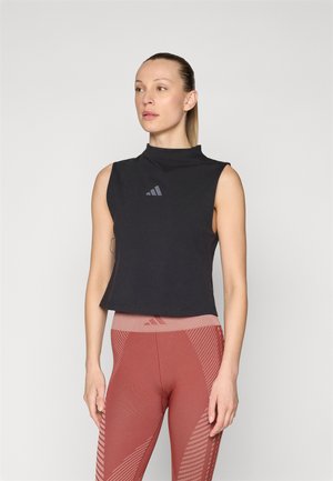Top negro sin mangas con un escote alto y un sutil detalle de logo. Combinado con leggings rojos texturizados que presentan un patrón geométrico.