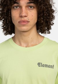 Světle zelené bavlněné tričko s šedým, zaobleným písmem "Element" na levé straně hrudi. Krátké rukávy, kulatý výstřih.