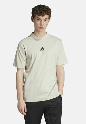 Camiseta de algodón beige claro con cuello redondo y mangas cortas, que presenta un pequeño logo negro de Adidas centrado en el pecho.