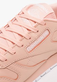 Rosa Reebok Classic-sneaker med textilsnörning, sydd läderdetalj och synlig Reebok-logotyp på sidan och på tungan.