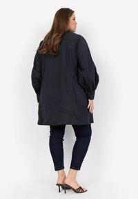 Camicia nera lunga con un taglio morbido, maniche a sbuffo e polsini abbottonati, abbinata a jeans skinny scuri e tacchi in stampa leopardata.