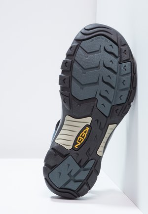 Gumowa podeszwa buta z głębokim bieżnikiem; cechuje się szaro-czarnymi kolorami, teksturowaną powierzchnią oraz wyraźnym żółtym logo "KEEN".