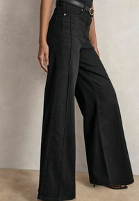 Pantalones vaqueros de tiro alto, anchos y negros con una textura suave, que cuentan con bolsillos frontales y una cinturilla reforzada. La tela es de mezclilla.