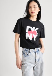 Svart bomull T-skjorte med 'DKNY' logo i hvitt og rosa. Avslappet passform med korte ermer. Båret med høytlivs lyseblå denim jeans.