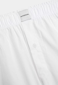 Białe bawełniane bokserki z elastycznym pasem i zapięciem na guziki. Metka jest podpisana "AUTOGRAPH." Gładka struktura bez wzorów.