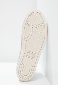 Bílá gumová podrážka tenisky Converse se strukturálním vzorem, zaoblenou špičkou a viditelným logem "CONVERSE ALL STAR."