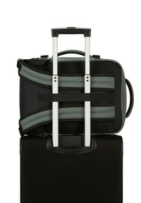 Maleta negra con un mango extensible, acompañada de una mochila verde y negra que presenta correas y detalles de malla.