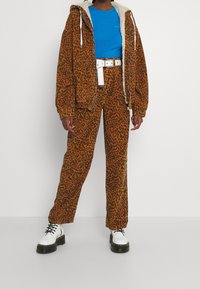 Orange leopardmönstrad jacka med fuskpälsfoder, ihopparad med matchande byxor och en blå ribbad topp. Vita grova snörstövlar kompletterar stilen.