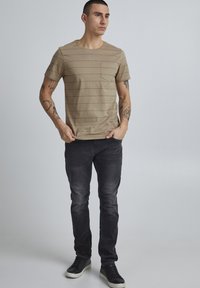 Kreemikaalune triibuline T-särk ümmarguse kaelusega ja taskuga, millele on sobitatud tumehall slim-fit teksapüksid ja mustad tennisetossud.