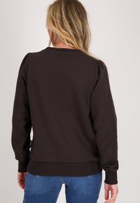 Bruine sweatshirt met een relaxte fit, geribde manchetten en zoom, met puffed schouders, zachte textuur en een label aan de linkerkant.