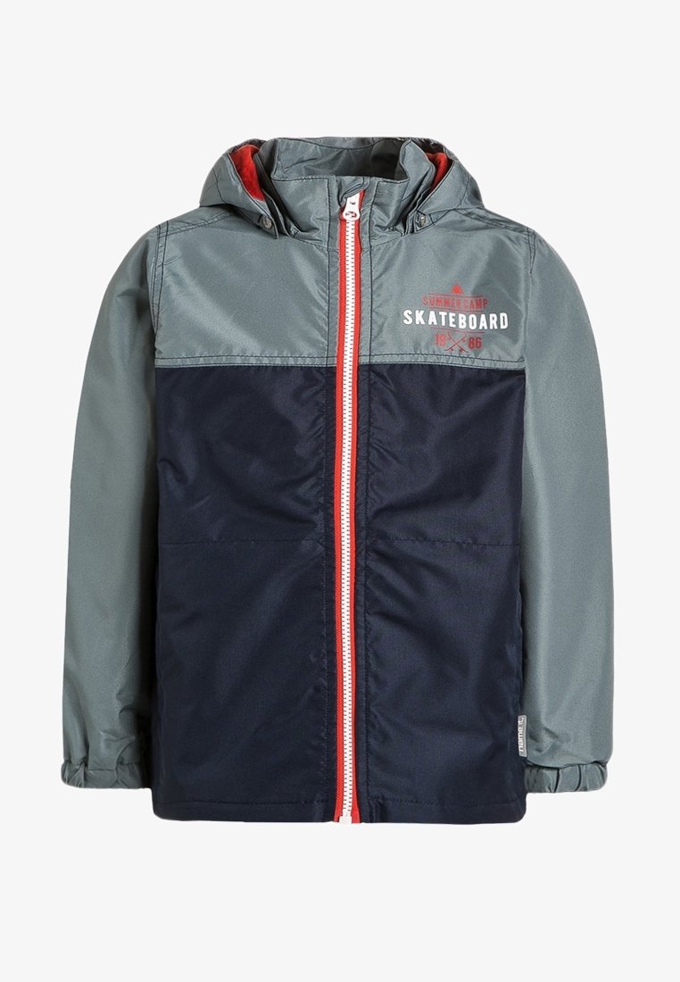 Veste imperméable avec une partie supérieure grise et une partie inférieure marine, fermeture éclair rouge, capuche et détail graphique "SKATEBOARD" sur le devant.