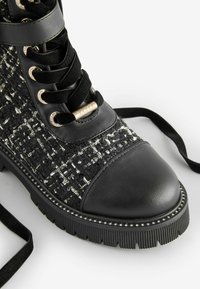 Stivaletto con tomaia in tweed nero e dettagli argentati, punta in pelle nera e suola in gomma testurizzata con dettagli borchiati.