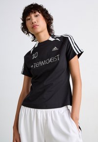 Black short-sleeve athletic shirt featuring white accents, number 10, and "+TEAMGEIST" in silver. Fabric is smooth, with a relaxed fit.