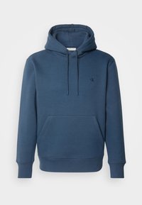 Sweat à capuche bleu avec poche kangourou à l'avant et petit logo "cK" sur la poitrine gauche, présenté sur fond blanc.