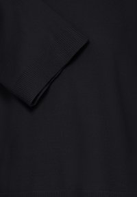 Gros plan sur un tissu noir tricoté montrant une manche longue pliée avec un détail de manchette côtelée.