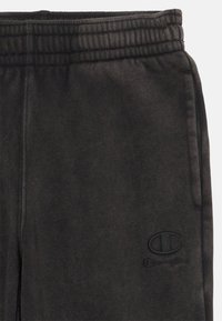 Čierne tepláky vyrobené z jemného materiálu, s elastickým pásom a tonálnym vyšívaným logom na dolnej ľavej strane.