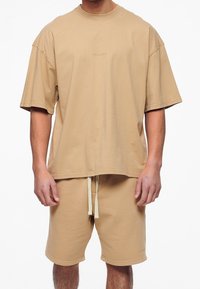 Beige oversized t-shirt med korte ærmer og rund hals, parret med matchende beige shorts med elastisk talje og snøre.