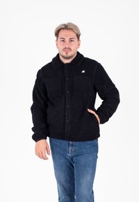 Zwarte fleecetrui met een kraag, twee voorzakken, knoopsluiting en een lichtgekleurde logo-accent op de borst.
