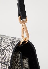 Black leather strap attached to a white and black patterned bag, featuring a gold-colored metal clasp and a smooth texture.