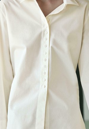 Close-up of a person wearing a cream-colored button-up shirt with a pointed collar, showing buttons aligned down the front.
